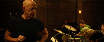 Movie still from “Whiplash” (2014), directed by Damien Chazelle – A man standing in front of a drum set in a room; Medium shot, Over the shoulder angle