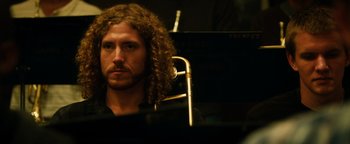 Movie still from “Whiplash” (2014), directed by Damien Chazelle – A man with long curly hair sitting in front of an instrument; Close Up shot, Low angle
