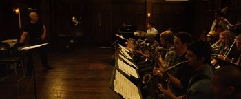 Movie still from “Whiplash” (2014), directed by Damien Chazelle – A group of people sitting in a room playing musical instruments; Extreme Wide shot, High angle