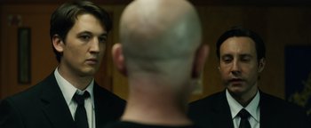 Movie still from “Whiplash” (2014), directed by Damien Chazelle – A man with a bald head is looking at another man in a suit; Close Up shot, Over the shoulder angle