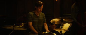 Movie still from “Whiplash” (2014), directed by Damien Chazelle – A man is playing drums while another man looks on; Medium shot, Over the shoulder angle