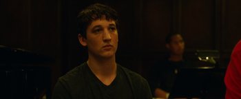 Movie still from “Whiplash” (2014), directed by Damien Chazelle – A young man is standing in front of a table; Close Up shot, Over the shoulder angle