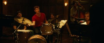 Movie still from “Whiplash” (2014), directed by Damien Chazelle – A man is playing drums in front of a group of people; Medium shot, Over the shoulder angle