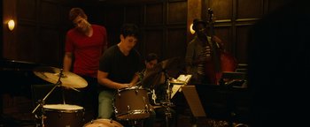 Movie still from “Whiplash” (2014), directed by Damien Chazelle – A group of people playing drums in a room; Medium shot, Over the shoulder angle