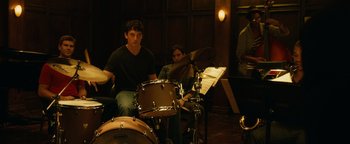 Movie still from “Whiplash” (2014), directed by Damien Chazelle – A man sitting on top of a drum set next to a woman; Medium shot, High angle
