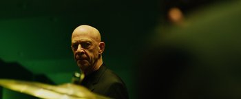 Movie still from “Whiplash” (2014), directed by Damien Chazelle – A man with a shaved head and a black shirt; Close Up shot, Over the shoulder angle