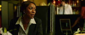 Movie still from “Whiplash” (2014), directed by Damien Chazelle – A woman sitting in a chair wearing a black suit; Close Up shot, Over the shoulder angle