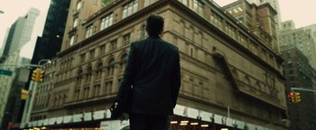 Movie still from “Whiplash” (2014), directed by Damien Chazelle – A man in a black suit is standing in front of a building; Extreme Wide shot, Low angle