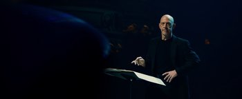Movie still from “Whiplash” (2014), directed by Damien Chazelle – A man in a black jacket is holding a sheet of paper; Medium shot, Low angle