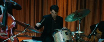 Movie still from “Whiplash” (2014), directed by Damien Chazelle – A man is playing a drum set in a room; Medium shot, Over the shoulder angle