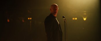Movie still from “Whiplash” (2014), directed by Damien Chazelle – A man standing in front of a microphone in a dark room; Medium shot, Low angle