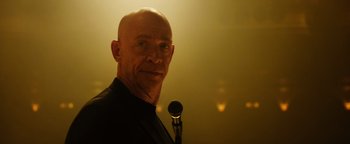 Movie still from “Whiplash” (2014), directed by Damien Chazelle – A man with a bald head holding a microphone in front of him; Close Up shot, Over the shoulder angle