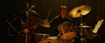 Movie still from “Whiplash” (2014), directed by Damien Chazelle – A young man playing drums in front of a group of other people; Medium shot, Over the shoulder angle