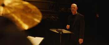 Movie still from “Whiplash” (2014), directed by Damien Chazelle – A man standing at a podium in front of an instrument; Medium shot, Low angle