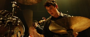 Movie still from “Whiplash” (2014), directed by Damien Chazelle – A young man holding a violin while another man plays the violin; Close Up shot, Over the shoulder angle