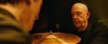 Movie still from “Whiplash” (2014), directed by Damien Chazelle – A man standing in front of a cymbal in front of another man; Close Up shot, Over the shoulder angle