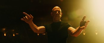 Movie still from “Whiplash” (2014), directed by Damien Chazelle – A bald man is holding his arm out in front of him; Medium shot, Low angle