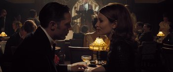 Movie still from “Legend” (2015), directed by Brian Helgeland – A man and a woman sitting at a table with a glass of wine; Medium shot, Over the shoulder angle