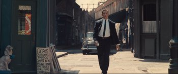 Movie still from “Legend” (2015), directed by Brian Helgeland – A man in a suit and tie walking down a street; Medium shot, Low angle