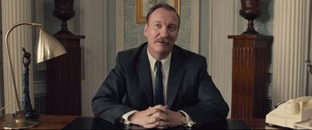 Movie still from “Legend” (2015), directed by Brian Helgeland – A man sitting at a table wearing a suit and tie; Close Up shot, Low angle