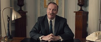 Movie still from “Legend” (2015), directed by Brian Helgeland – A man sitting at a table wearing a suit and tie; Close Up shot, Low angle