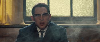 Movie still from “Legend” (2015), directed by Brian Helgeland – A man in a suit and tie with glasses; Close Up shot, Over the shoulder angle