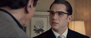 Movie still from “Legend” (2015), directed by Brian Helgeland – A man in a suit and glasses looking at another man in a suit and glasses; Close Up shot, Over the shoulder angle