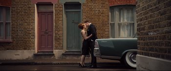 Movie still from “Legend” (2015), directed by Brian Helgeland – A man and a woman kissing in front of an old car; Wide shot, Low angle