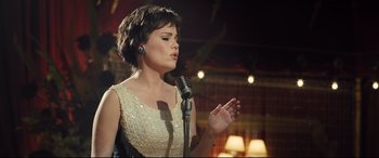 Movie still from “Legend” (2015), directed by Brian Helgeland – A woman in a white dress is singing into a microphone; Medium shot, Low angle