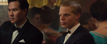 Movie still from “Legend” (2015), directed by Brian Helgeland – A young man in a suit and bow tie looking to his left; Close Up shot, Over the shoulder angle