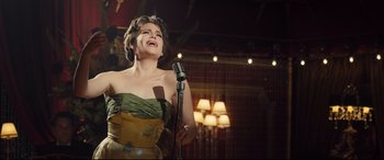 Movie still from “Legend” (2015), directed by Brian Helgeland – A woman in a strapless dress singing into a microphone; Medium shot, Low angle
