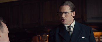 Movie still from “Legend” (2015), directed by Brian Helgeland – A man in a suit and tie standing in a dark room; Close Up shot, Over the shoulder angle