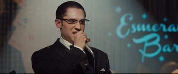Movie still from “Legend” (2015), directed by Brian Helgeland – A man in a suit and tie holding a microphone up to his mouth; Close Up shot, Low angle
