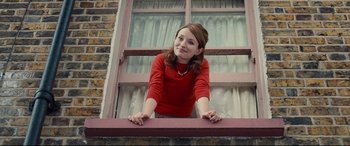 Movie still from “Legend” (2015), directed by Brian Helgeland – A woman in a red shirt leaning up against a window ledge; Medium shot, Low angle