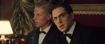 Movie still from “Legend” (2015), directed by Brian Helgeland – A man in a suit and tie next to another man in a suit and tie; Close Up shot, Over the shoulder angle