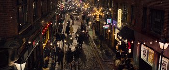 Movie still from “Legend” (2015), directed by Brian Helgeland – A busy city street at night lit up by street lights; Extreme Wide shot, High angle