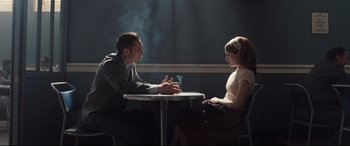 Movie still from “Legend” (2015), directed by Brian Helgeland – A man and a woman sitting at a table talking to each other; Medium shot, Over the shoulder angle