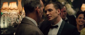 Movie still from “Legend” (2015), directed by Brian Helgeland – A man in a suit talks to another man in a suit; Close Up shot, Over the shoulder angle