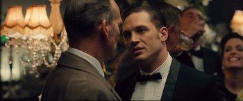 Movie still from “Legend” (2015), directed by Brian Helgeland – A man in a suit and bow tie talking to another man in a suit and bow tie; Close Up shot, Over the shoulder angle