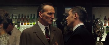 Movie still from “Legend” (2015), directed by Brian Helgeland – A man in a suit talking to another man in a suit and tie; Close Up shot, Over the shoulder angle