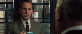 Movie still from “Legend” (2015), directed by Brian Helgeland – A man in a suit and tie holding a coffee mug; Close Up shot, Over the shoulder angle
