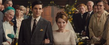 Movie still from “Legend” (2015), directed by Brian Helgeland – A man and a woman standing next to each other in front of flowers; Medium shot, Over the shoulder angle