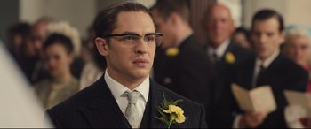 Movie still from “Legend” (2015), directed by Brian Helgeland – A man in a suit and tie holding a yellow flower; Close Up shot, Over the shoulder angle