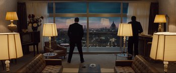 Movie still from “Legend” (2015), directed by Brian Helgeland – A man in a suit standing in front of a large window; Wide shot, Low angle