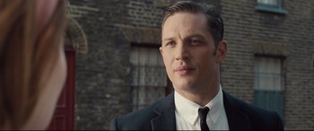 Movie still from “Legend” (2015), directed by Brian Helgeland – A man wearing a suit and tie in front of a brick building; Close Up shot, Over the shoulder angle