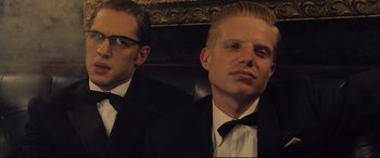 Movie still from “Legend” (2015), directed by Brian Helgeland – A man in a suit and tie sitting next to another man in a suit and tie; Close Up shot, Low angle