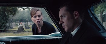 Movie still from “Legend” (2015), directed by Brian Helgeland – A man and a woman looking in a car window; Medium shot, Over the shoulder angle