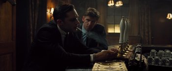 Movie still from “Legend” (2015), directed by Brian Helgeland – Two men in business suits sitting at a table; Medium shot, Low angle