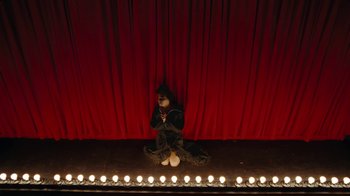 Movie still from “Lemonade” (2016), directed by Mark Romanek – A person sitting on a stage in front of a red curtain; Wide shot, High angle