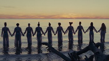 Movie still from “Lemonade” (2016), directed by Mark Romanek – A group of people standing in the water holding hands; Extreme Wide shot, Overhead angle